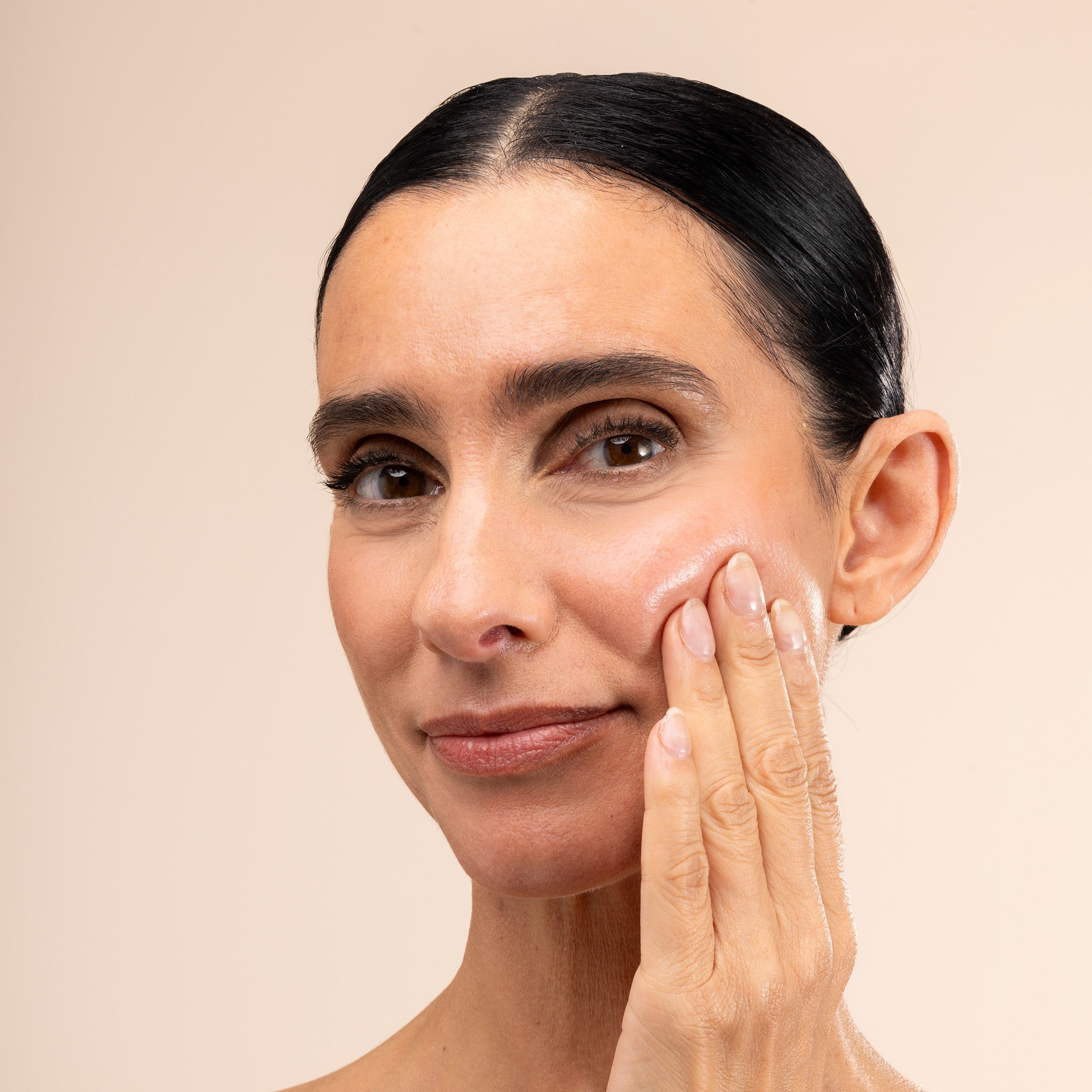 Woman applying Edelweiss Serum to her face against a beige background